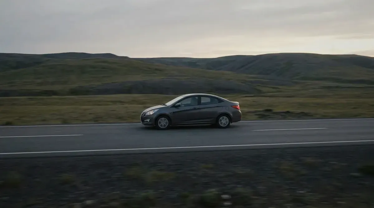 A compact car driving on an empty two-lane highway at dusk.