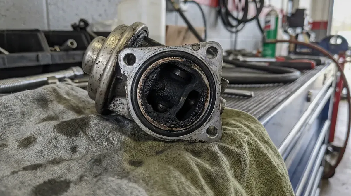 An EGR valve crusted with black carbon on a shop rag.