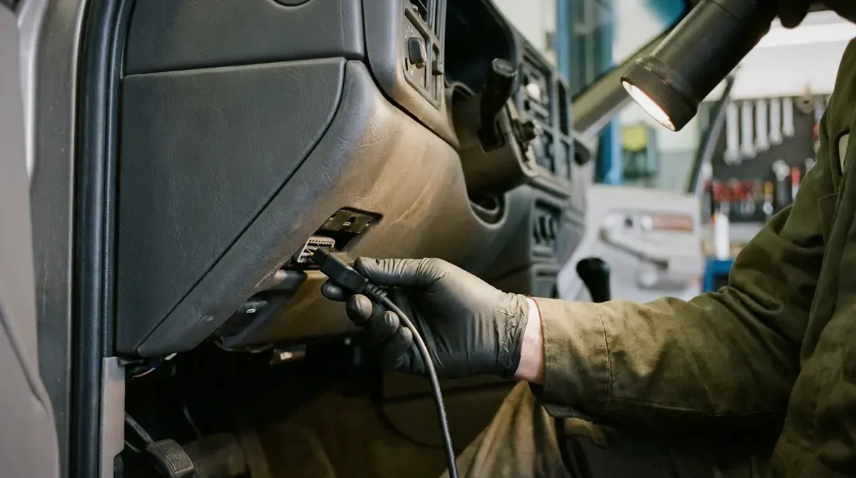 A diagnostic cable being plugged into the OBD port under a dashboard.