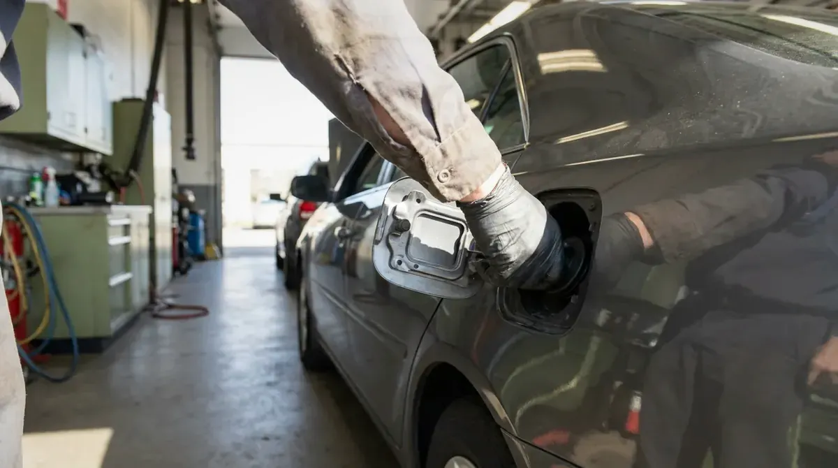 A hand twisting a gas cap shut on a car fuel filler.